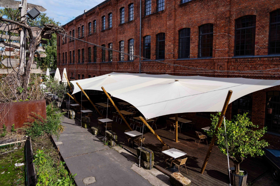 Ein langgezogenes Sonnensegel über der Terrasse des Sage Rstaurants in Berlin. Es dient den Gästen als Sonnenschutz.