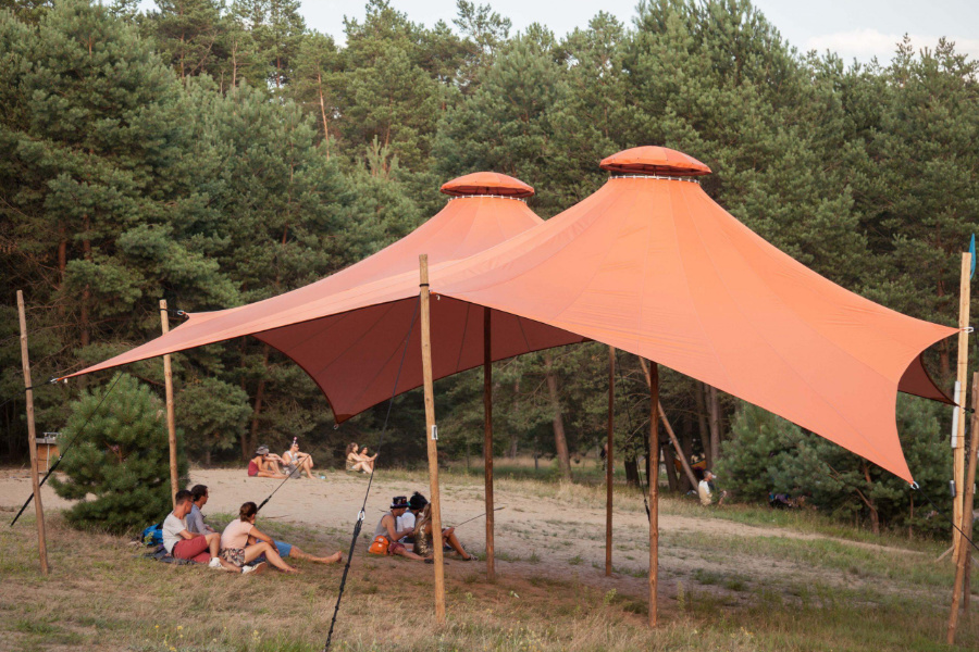 Ein ornges Zeltdach der Firma Stoffdach mit zwei Mittelstützen steht auf eine Waldlichtung auf dem Garbicz Festival. Es ist eine gemietete textiel Struktur.